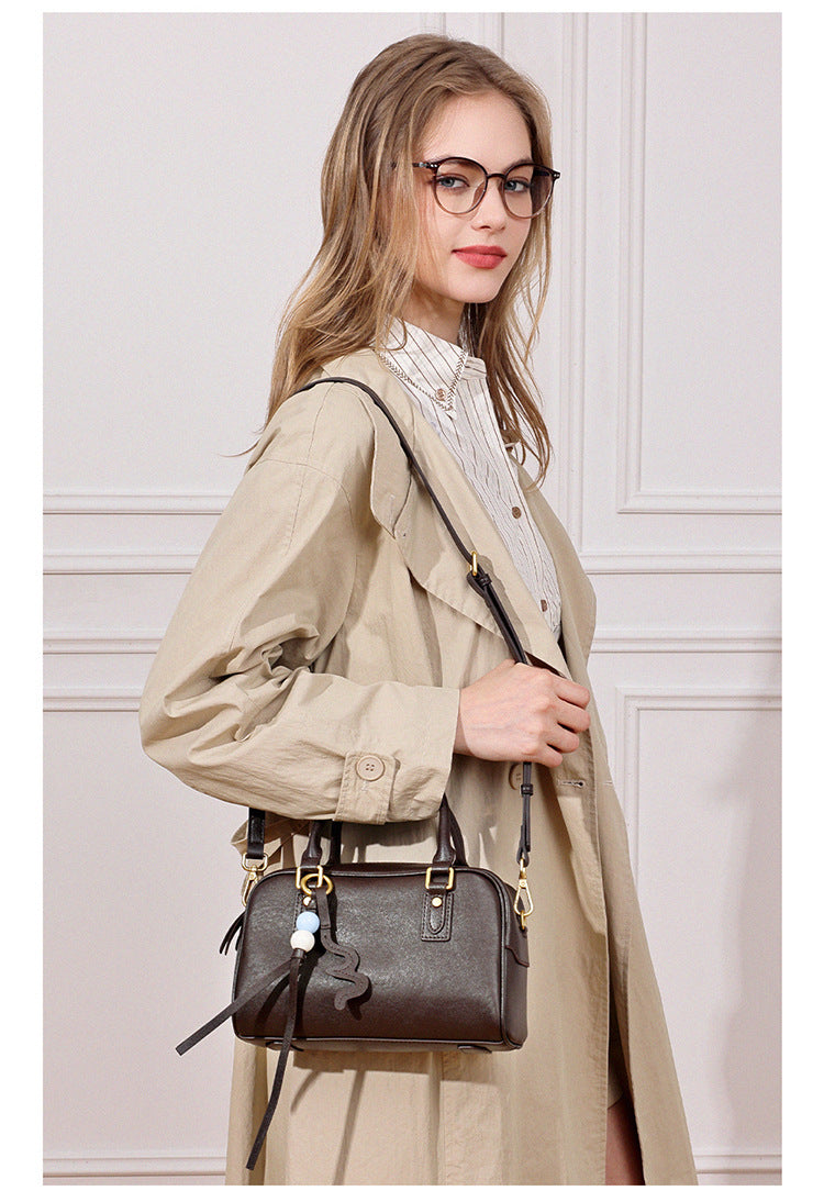 Model in a beige trench coat wearing a dark brown leather pillow crossbody bag