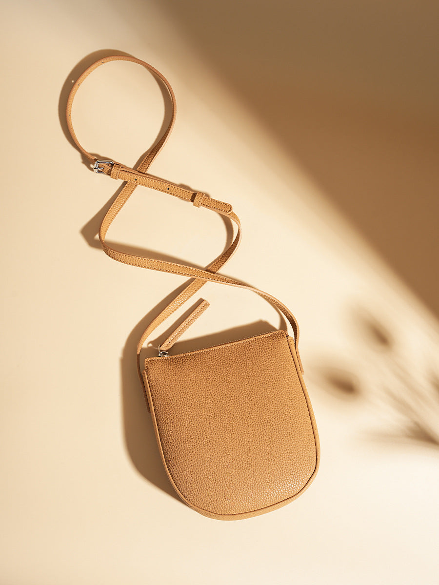 Flat lay of biscuit pebbled leather phone bag showing adjustable leather strap