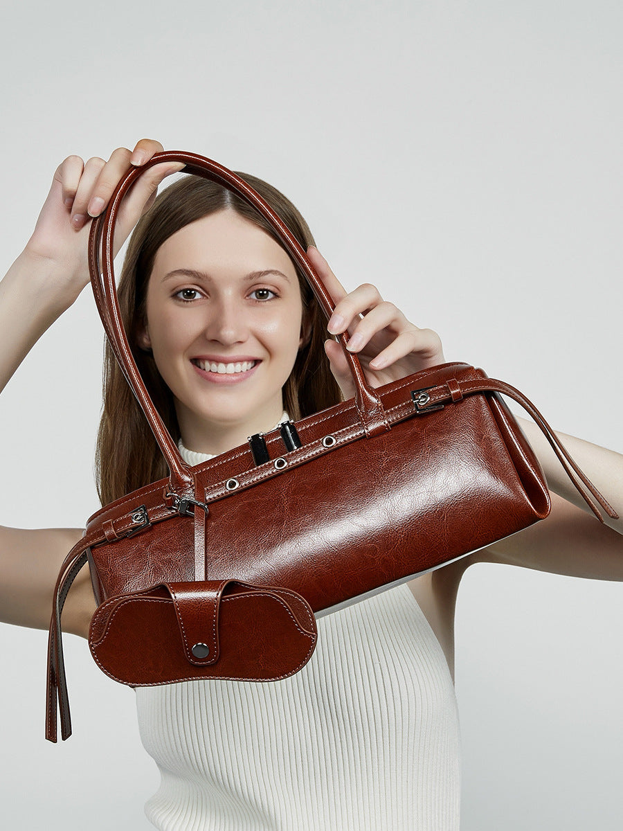 Smiling model holding brown leather barrel bag up to frame her face