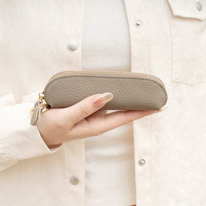 Grey pebbled cowhide coin purse held in hand showing smooth top zipper and slim profile