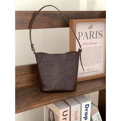 Brown bucket shoulder bag displayed on a wooden shelf