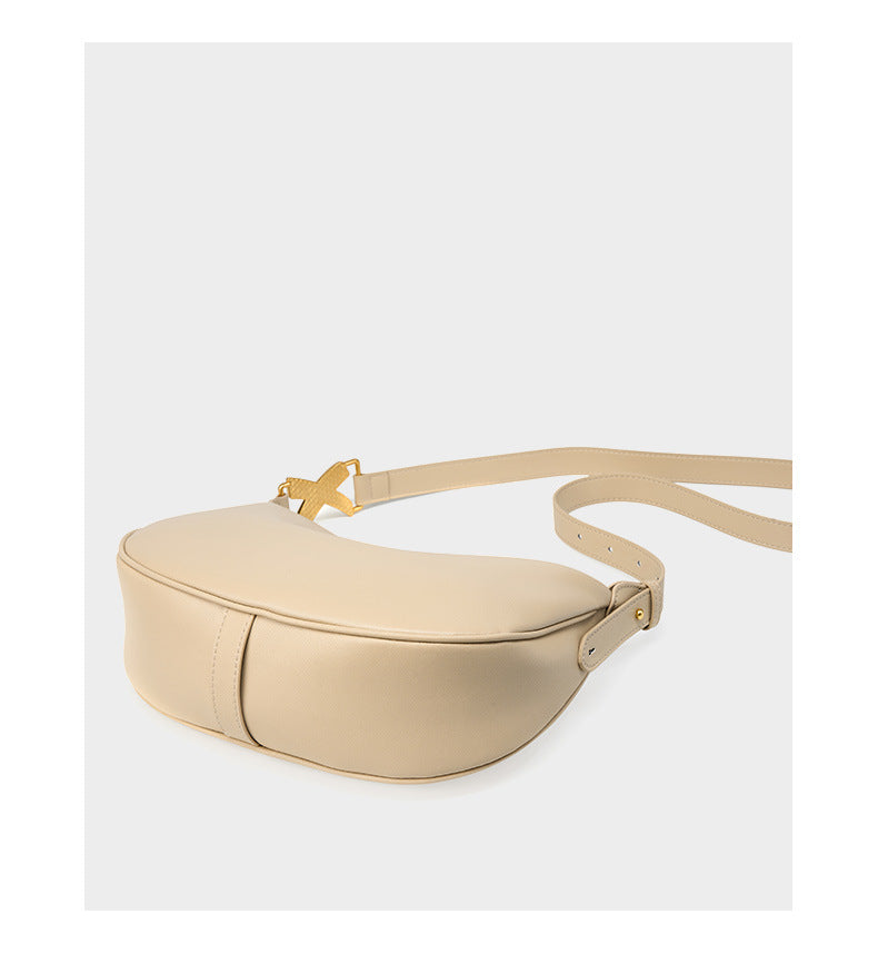 Off-white cowhide crescent underarm bag lying flat to show base and strap rivet