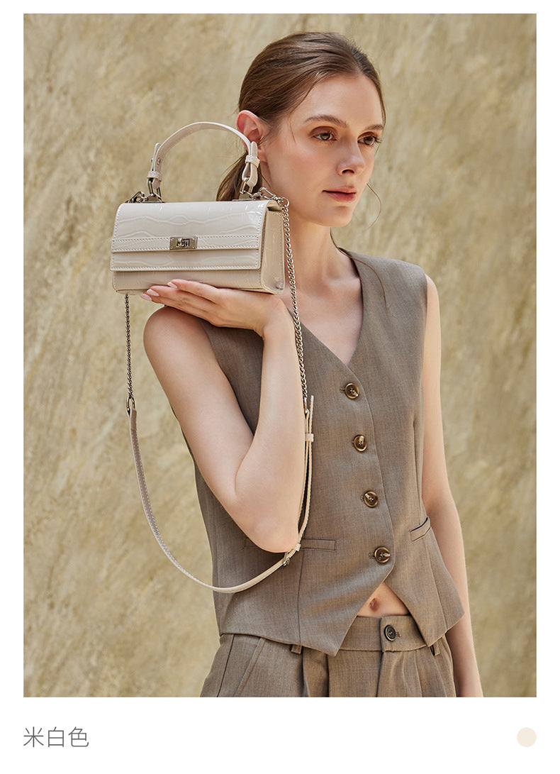 Model holding the cream white croco-embossed bag at her side against a textured wall