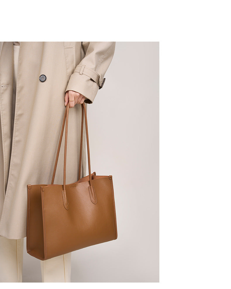 Golden brown leather tote bag carried by hand with a beige coat