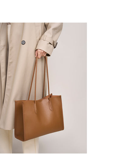 Golden brown leather tote bag carried by hand with a beige coat