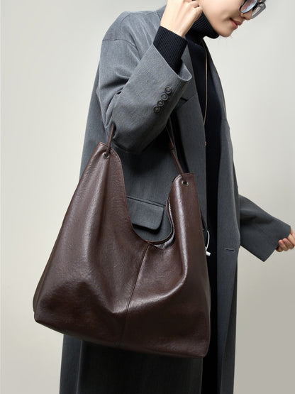 Brown hobo tote bag worn over the shoulder with a gray wool coat