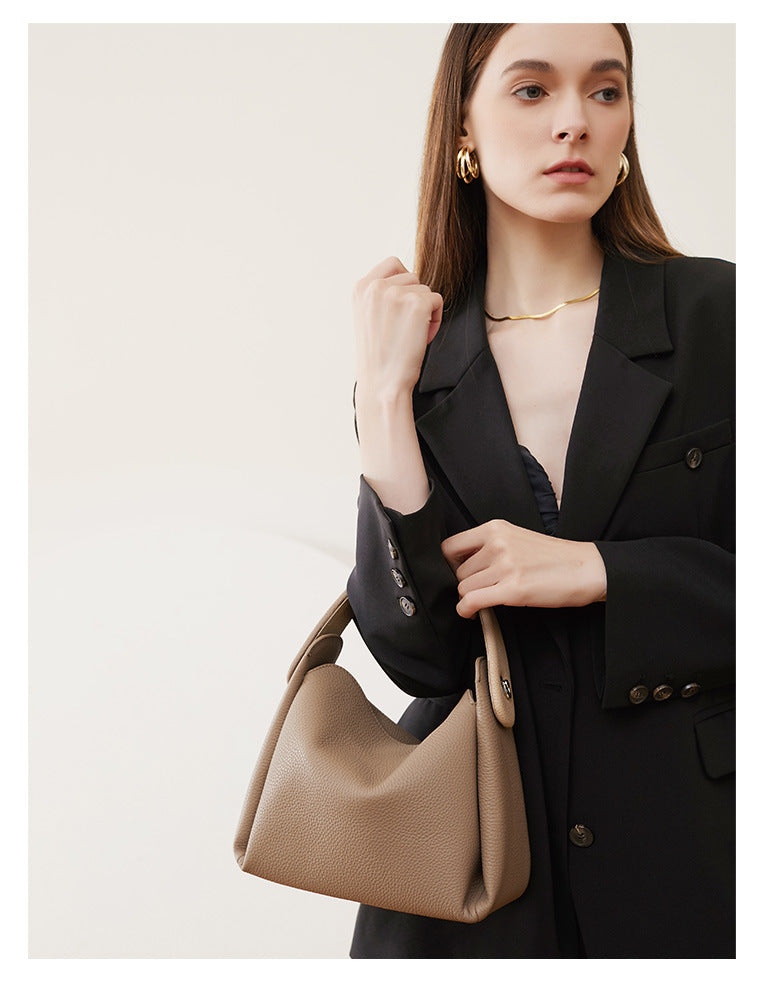 Model in black blazer holding pebbled leather handbag by top handle