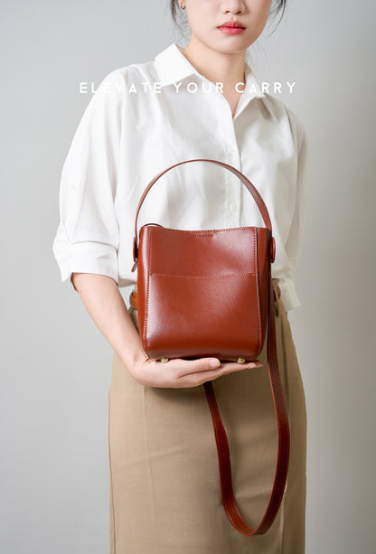 Brown leather bucket bag modeled with crossbody strap and tan trousers