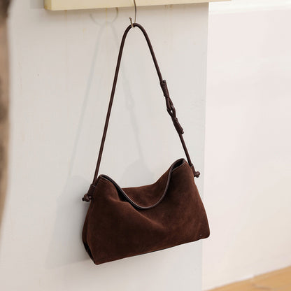 Dark coffee suede cowhide shoulder bag hanging against a light wall