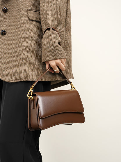 Model carrying brown leather mini bag by hand showcasing compact silhouette