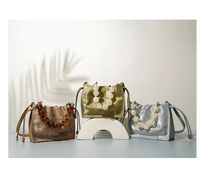 Three mini bucket bags in champagne, sage green, and silver displayed in a row