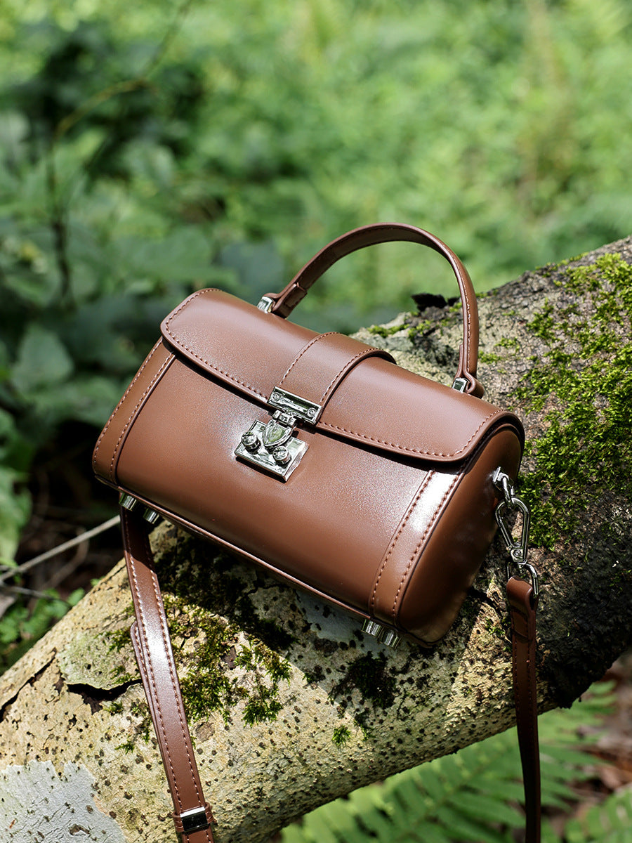 Brown cowhide leather mini box bag resting on a mossy log in a forest setting