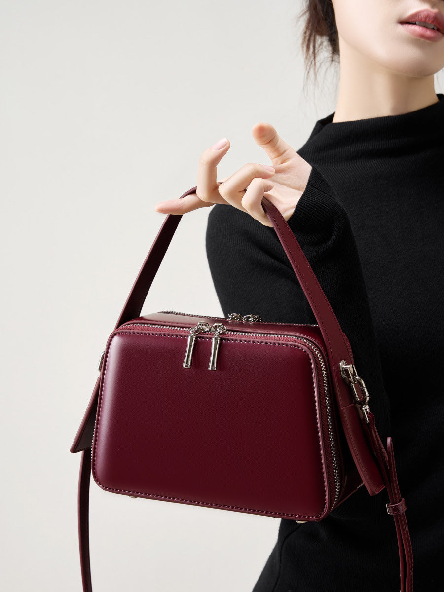 Model carrying the wine red leather crossbody bag by the top handle