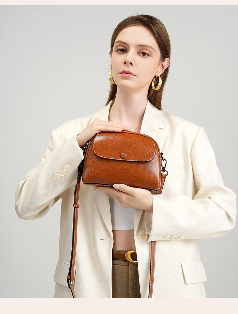 Model in cream blazer presenting caramel leather crossbody bag