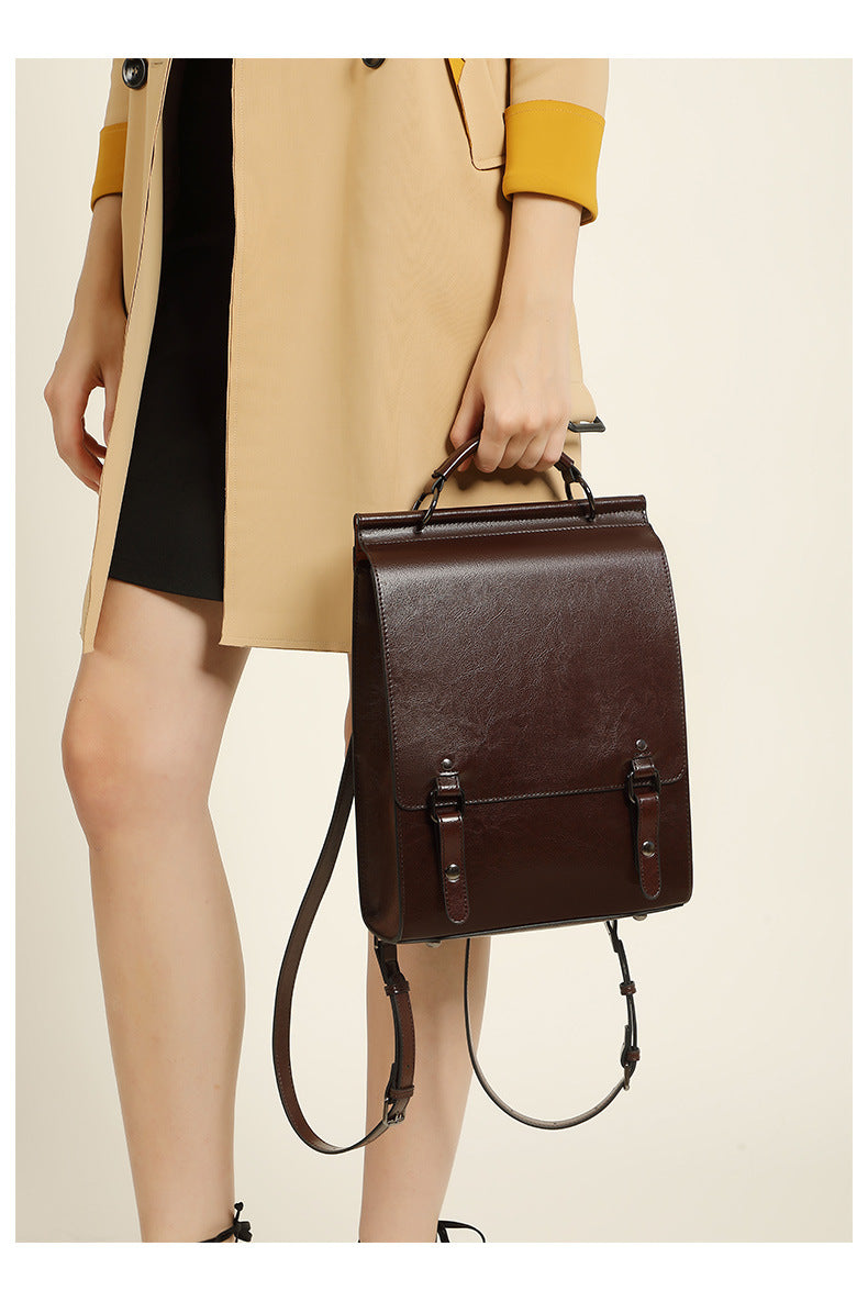 Model carrying brown backpack by top handle showing side profile