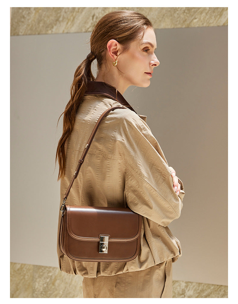 Brown leather messenger bag worn crossbody with trench coat