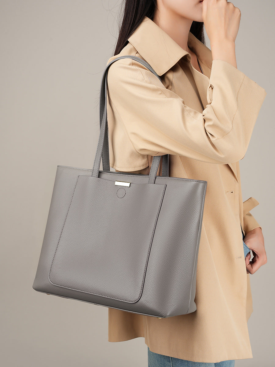 Model wearing beige trench coat holding dark gray leather tote bag