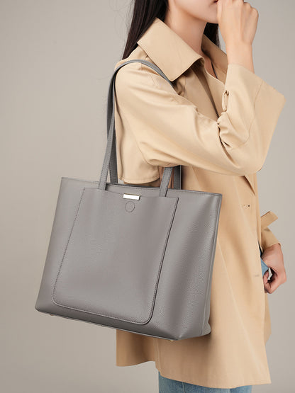 Model wearing beige trench coat holding dark gray leather tote bag