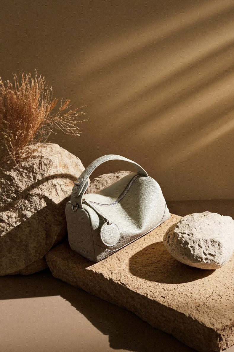 Ash white mini Boston bag displayed on rough stone with dried botanicals