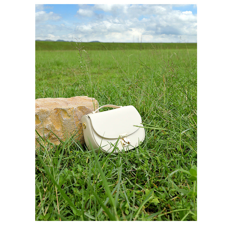Cream saddle bag resting in tall grass beside a stone