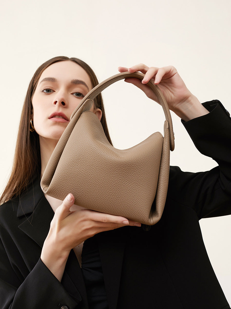 Model holding pebbled leather top-handle bag showing soft silhouette