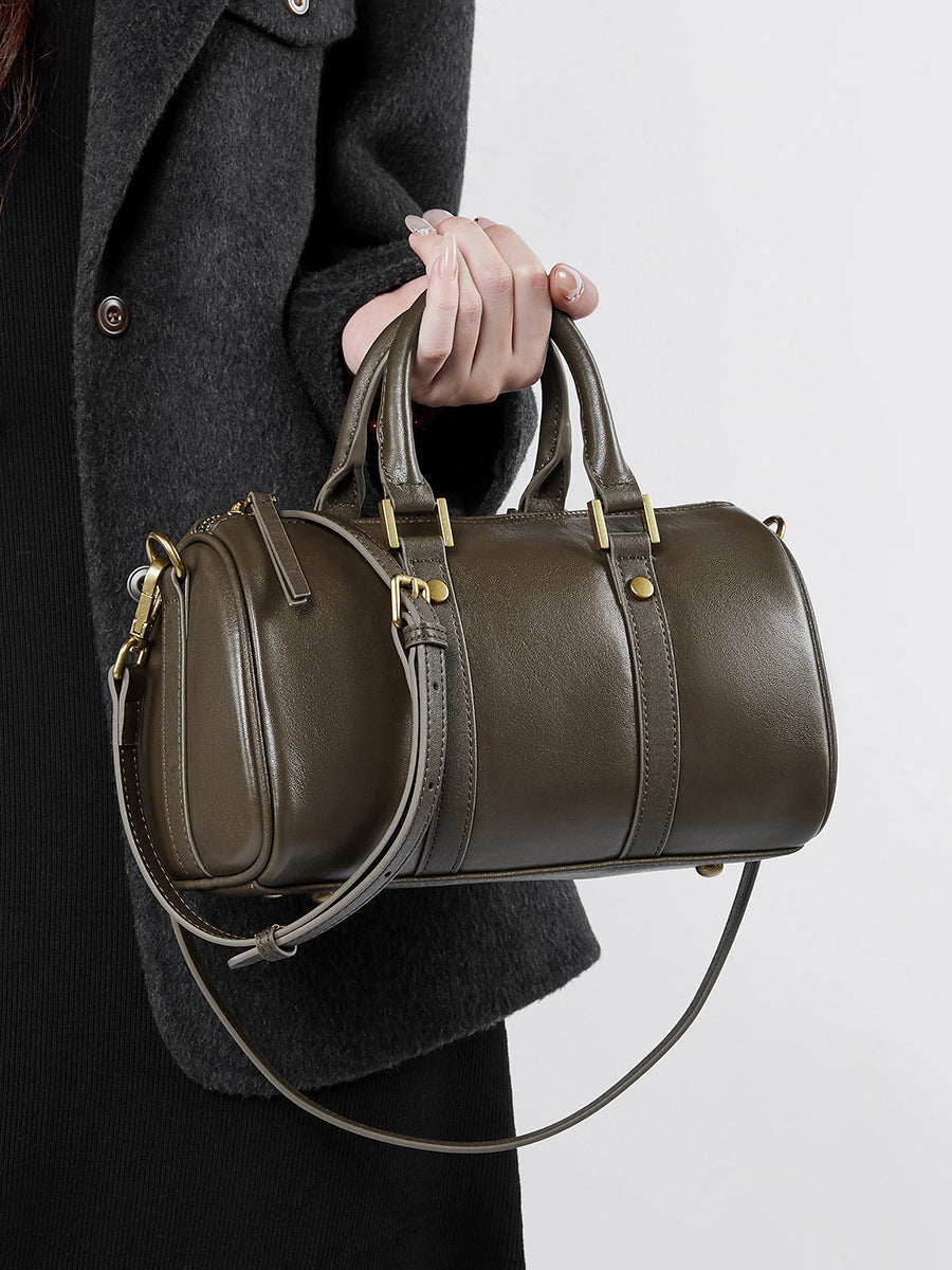 Olive green cowhide Boston bag held by top handle against dark coat