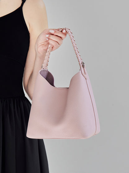Pink leather bucket bag held by the braided top handle, showing the scooped opening