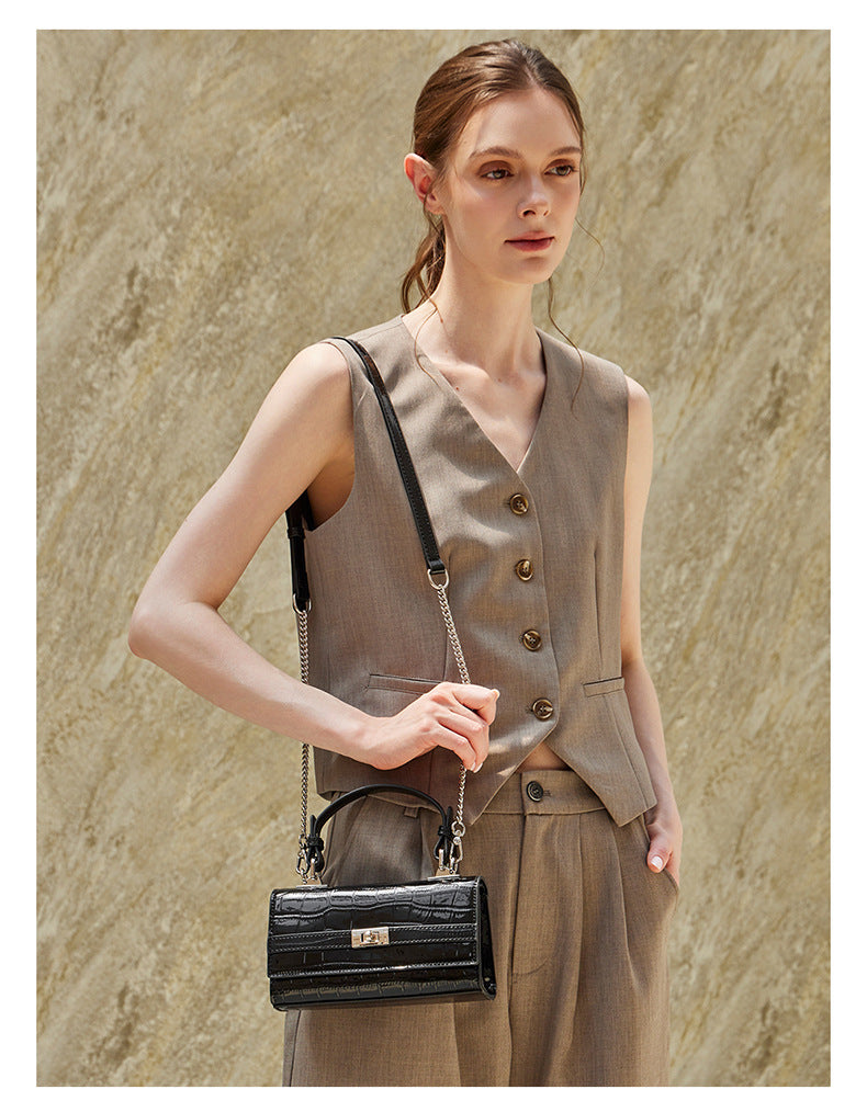 Model carrying the black croco-embossed bag crossbody with chain strap at her hip
