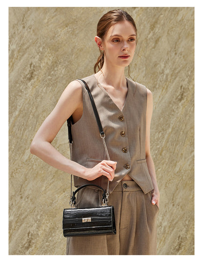 Model carrying the black croco-embossed bag crossbody with chain strap at her hip