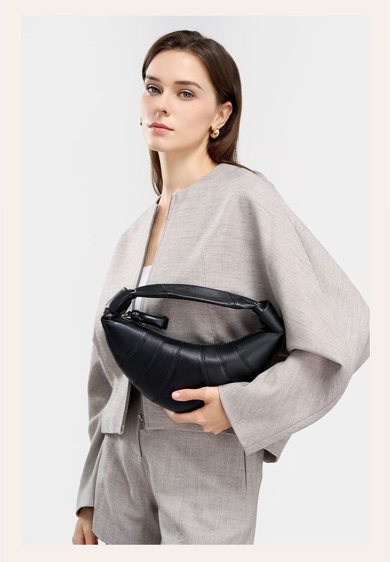 Close-up of model cradling black crescent bag against gray jacket