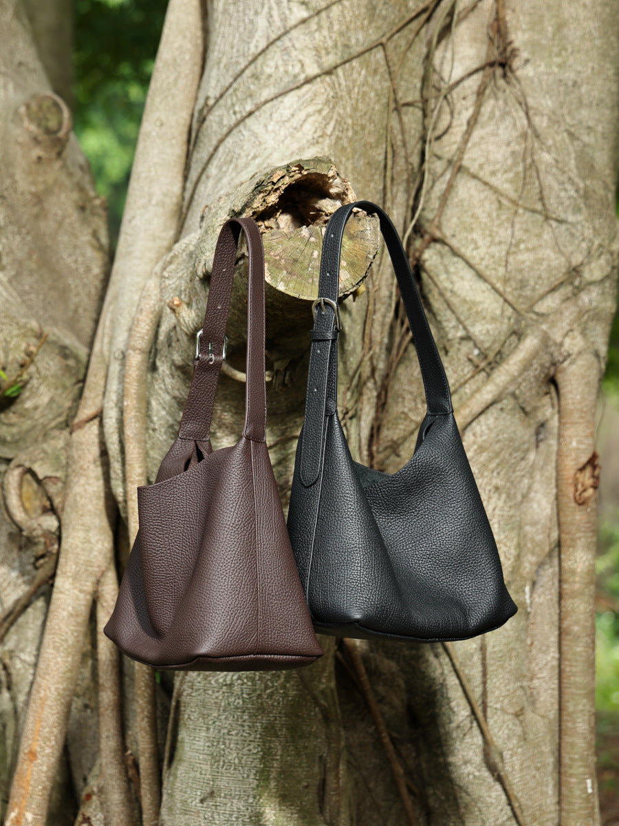 Black and coffee brown hobo bags hanging from a tree branch outdoors