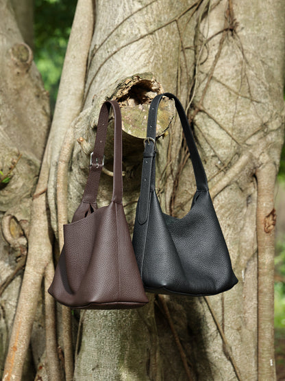 Black and coffee brown hobo bags hanging from a tree branch outdoors