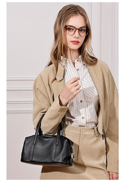 Model in beige jacket holding black bag indoors