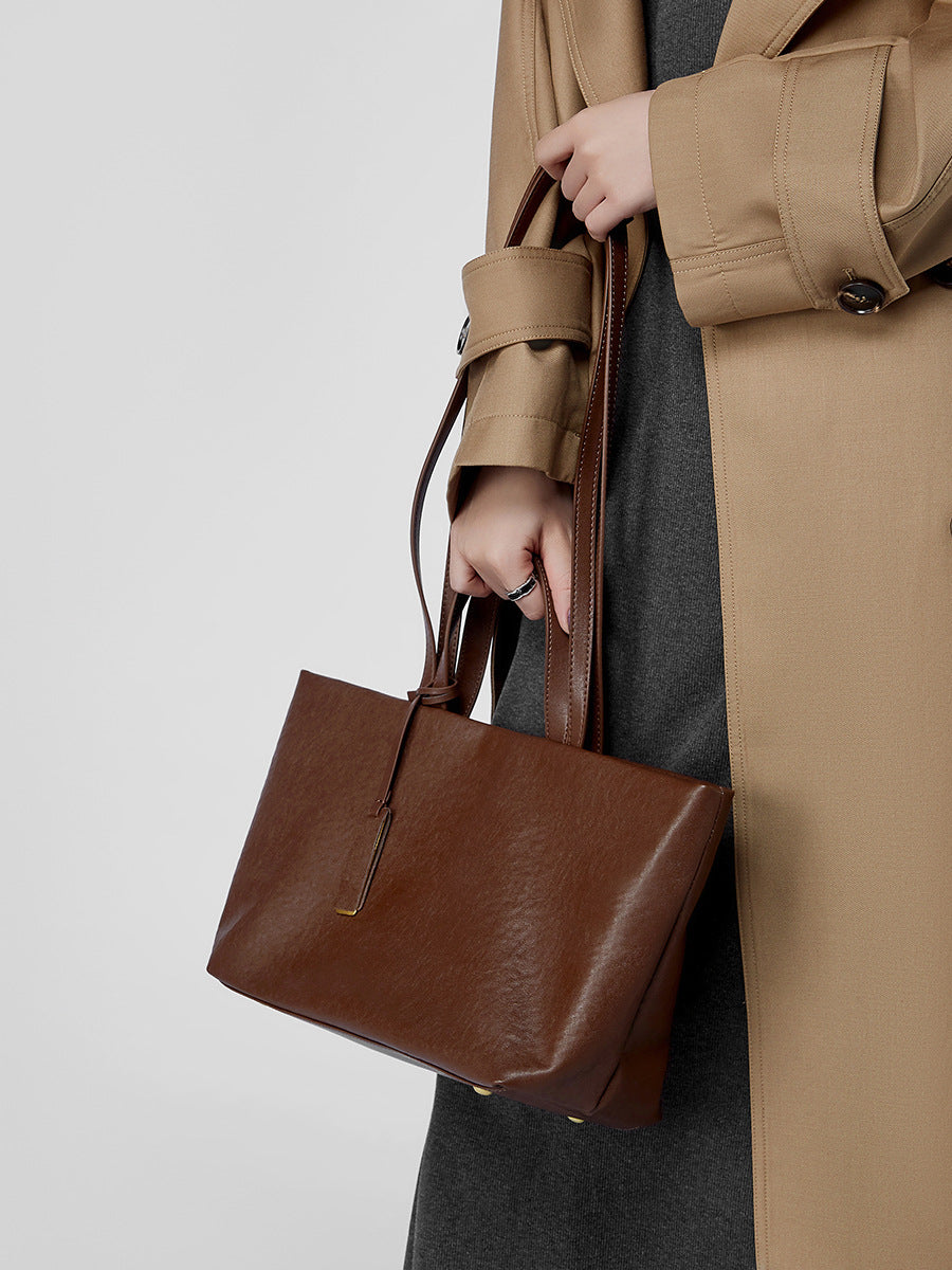Model in camel trench coat holding brown leather tote bag
