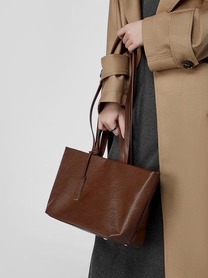 Model in camel trench coat holding brown leather tote bag