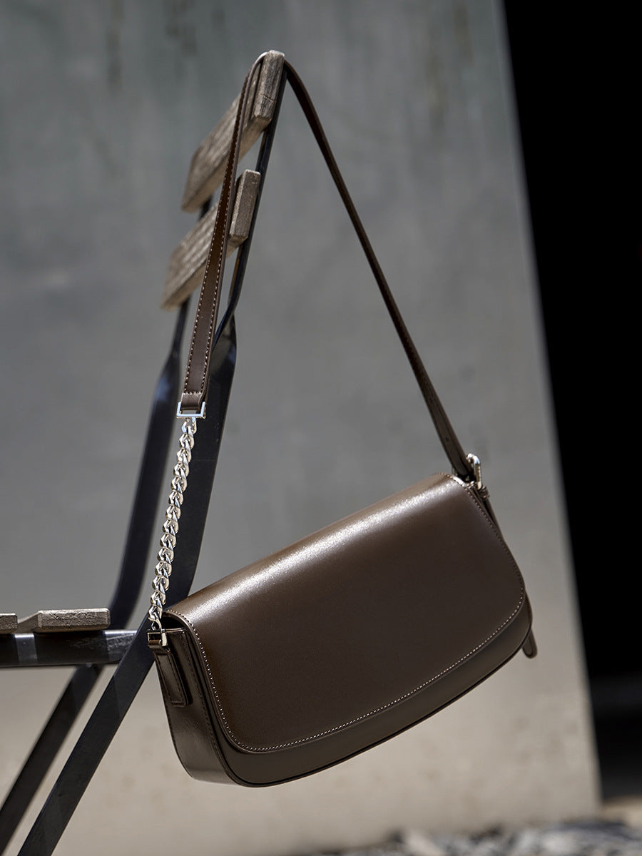 Brown leather baguette bag hanging on a metal stand showing flap and chain detail