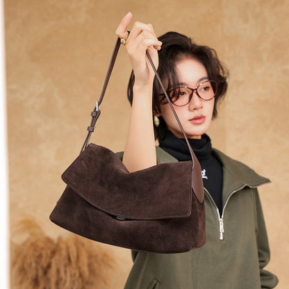 Dark brown suede bag displayed in a model's hand