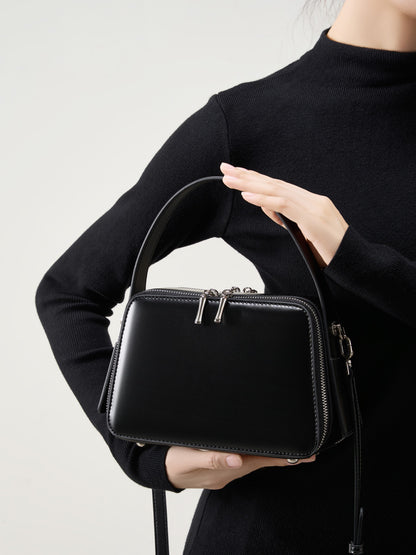 Model holding the black leather crossbody bag against a black top
