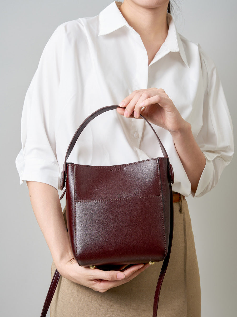 Woman holding coffee brown leather bucket bag against a white shirt