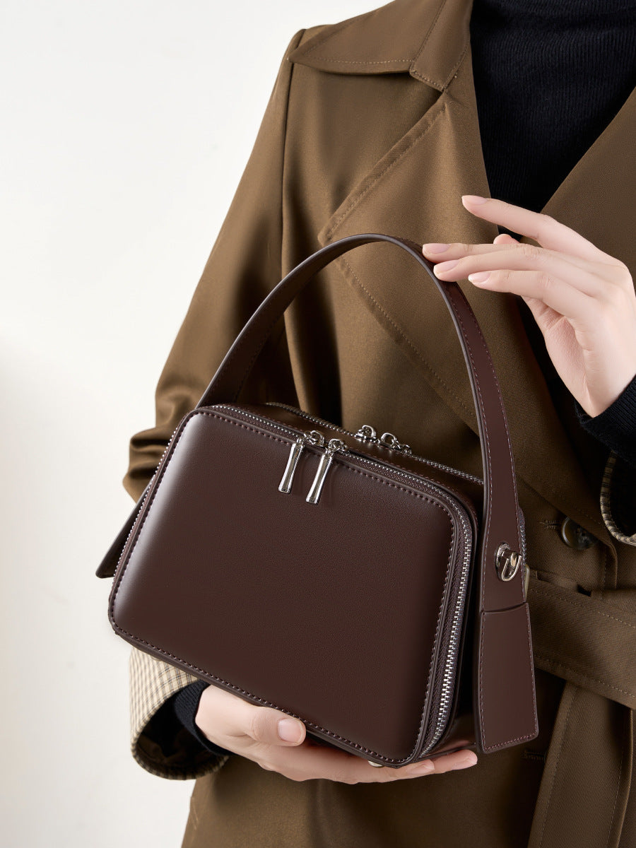 Model holding the coffee brown leather crossbody bag by the top handle