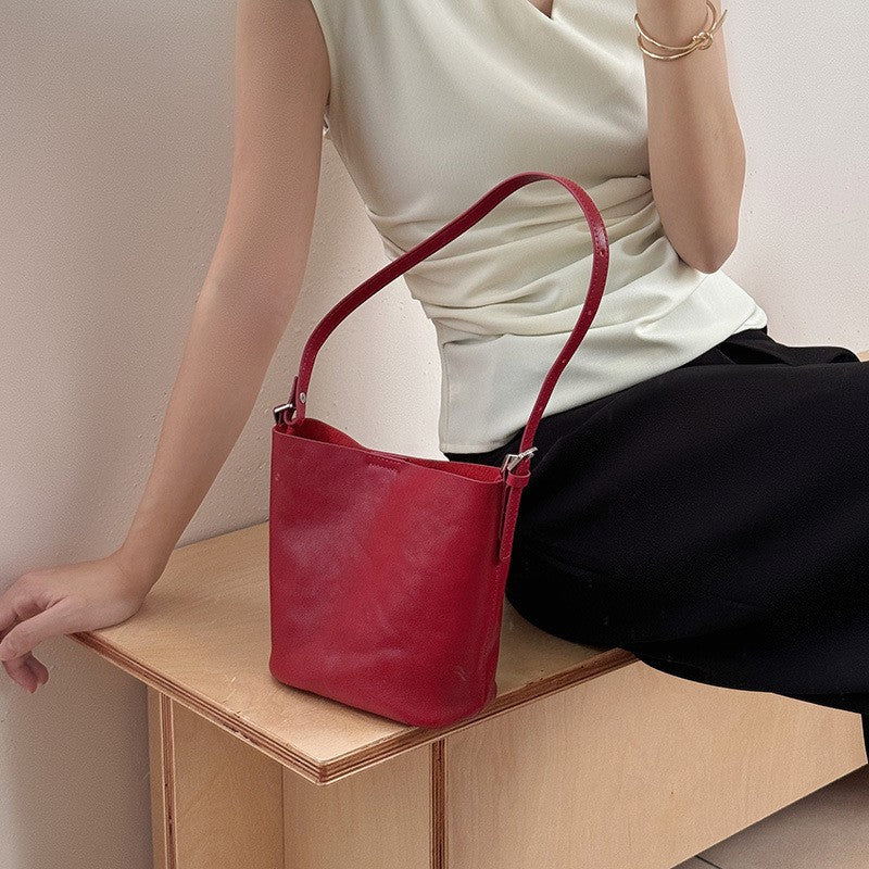 Burgundy leather bucket bag styled beside a seated model