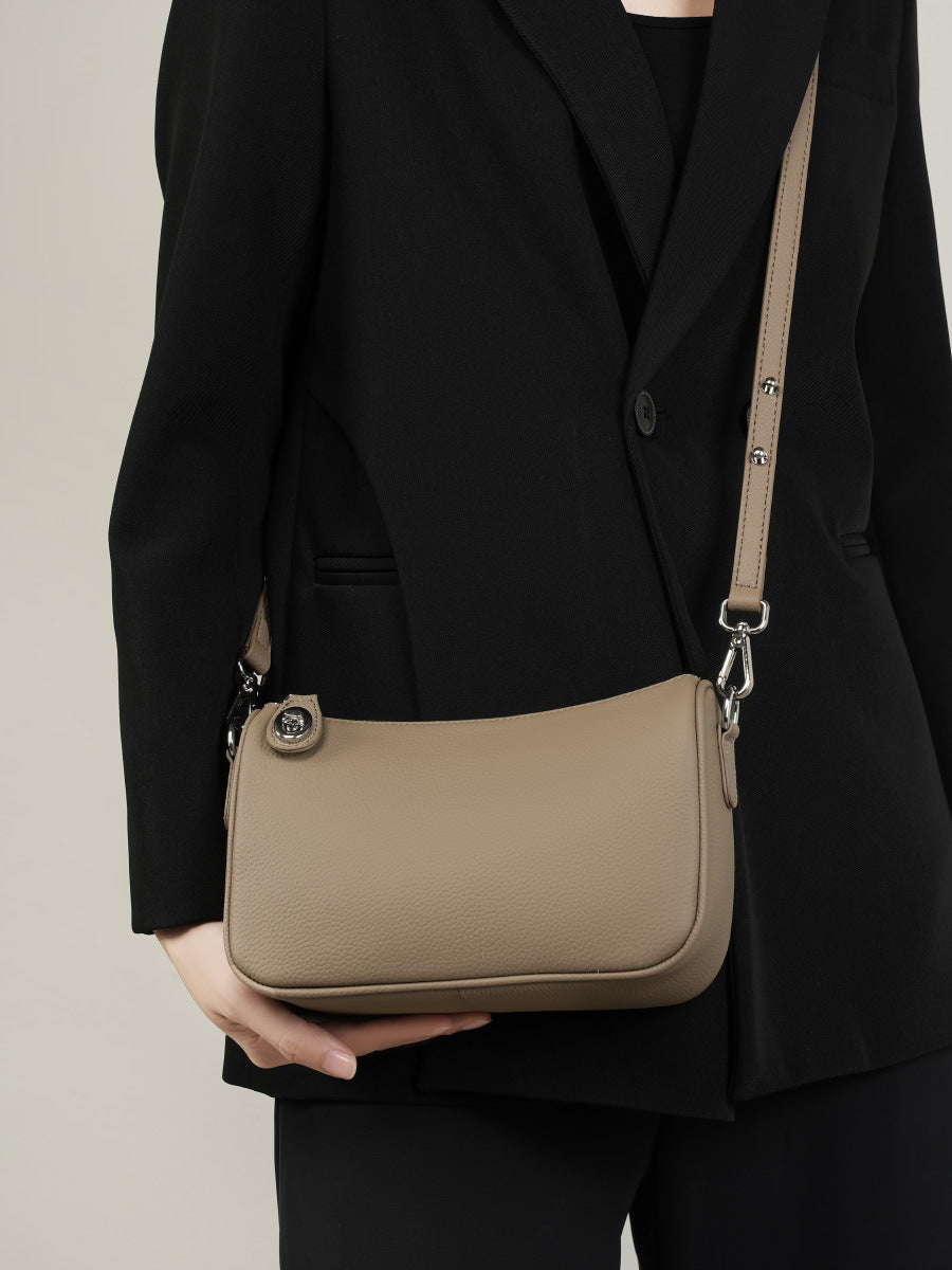 Taupe pebbled leather crossbody bag held under arm with black blazer