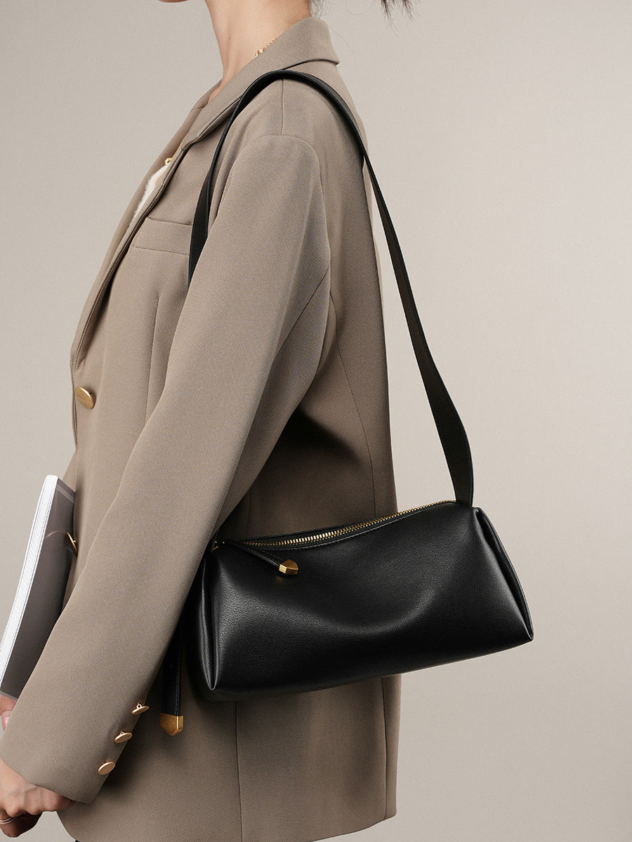 Black pillow crossbody bag worn on the shoulder with a beige blazer