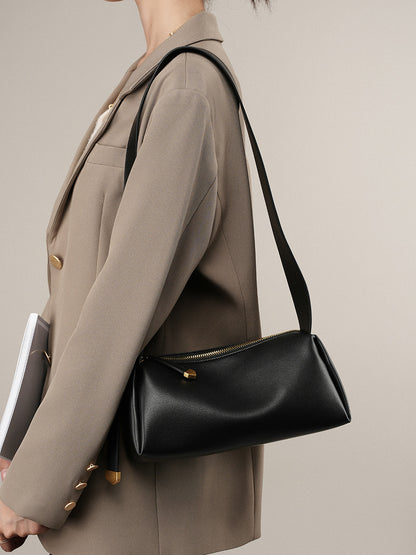 Black pillow crossbody bag worn on the shoulder with a beige blazer
