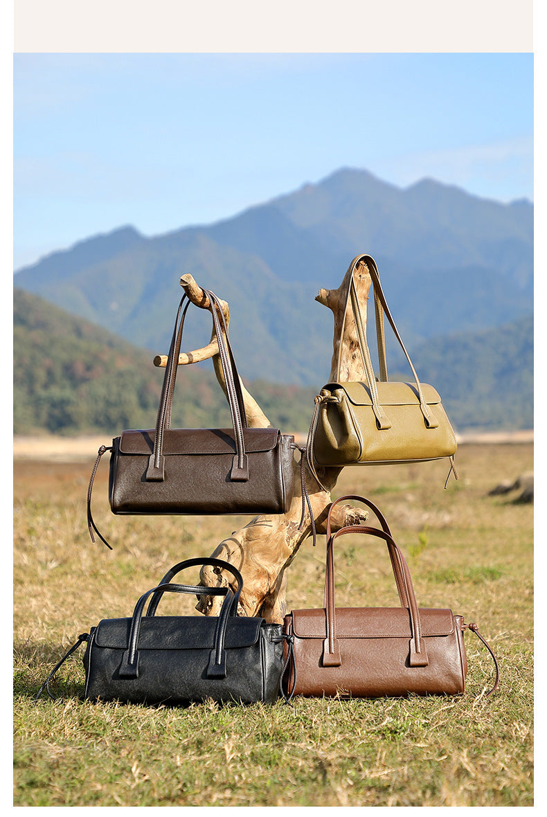 Four cowhide leather shoulder bags in coffee, olive, black, and brown displayed on grass