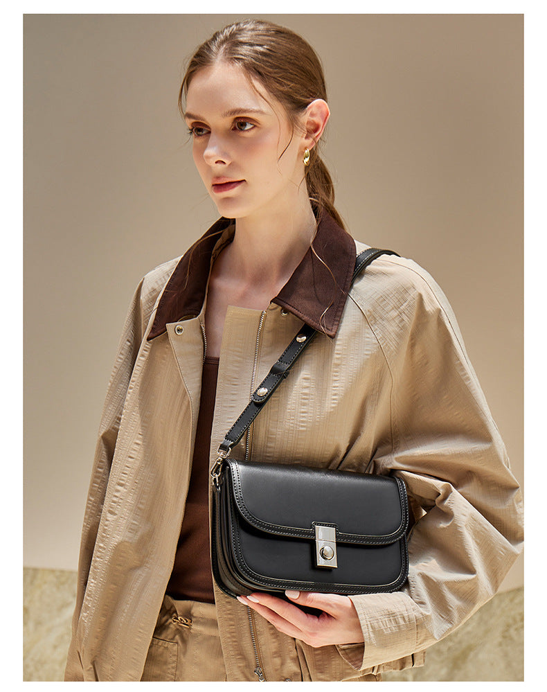 Black leather messenger bag worn crossbody with trench coat