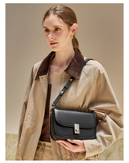 Black leather messenger bag worn crossbody with trench coat