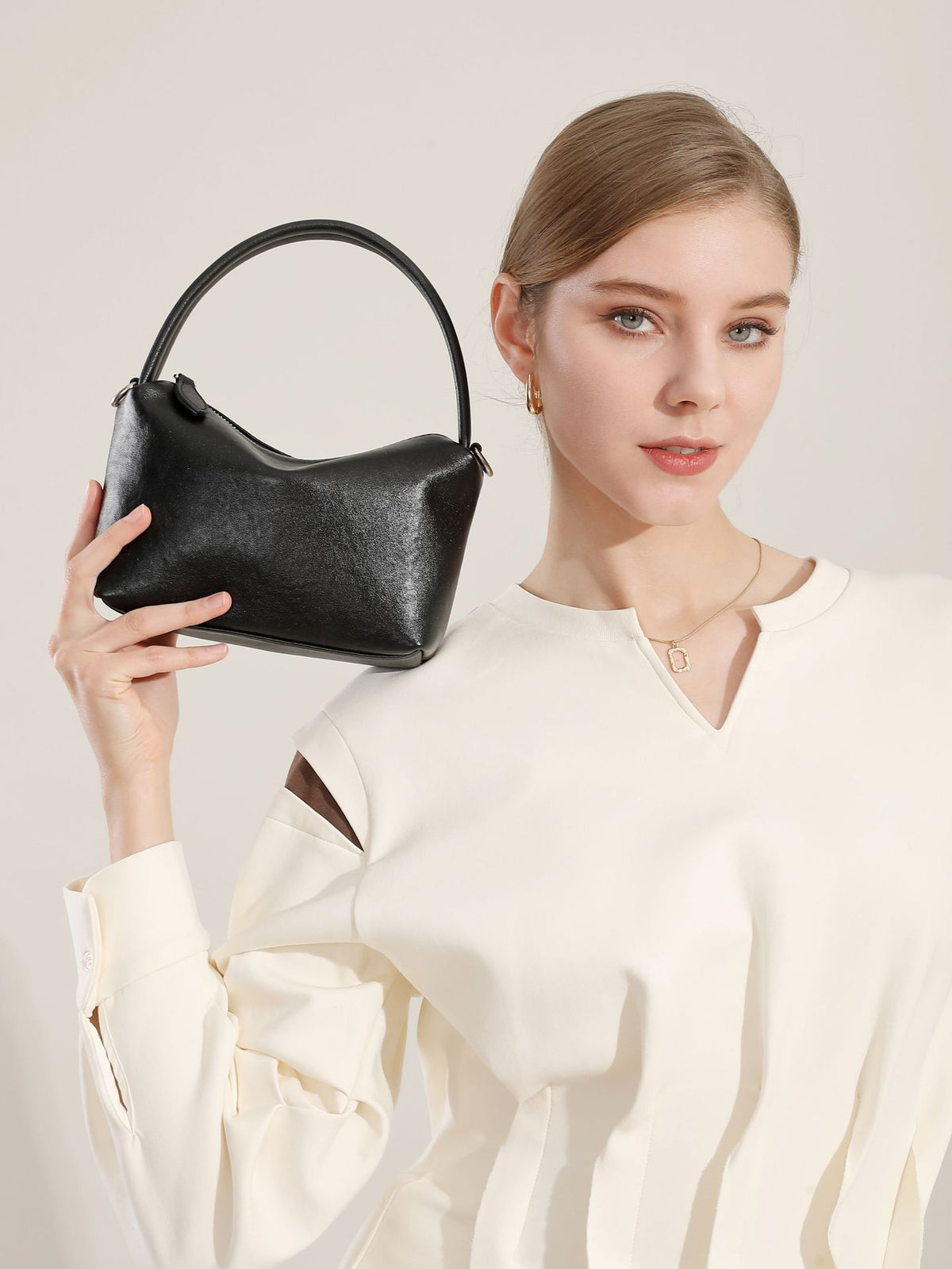 Black leather pillow bag held up by a model in a white top