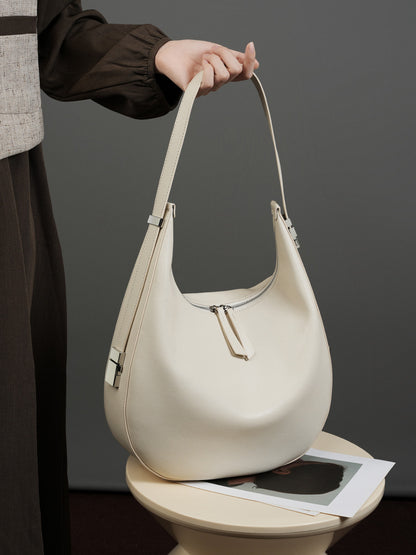Model in brown blouse and tweed vest holding the cream white cowhide leather crescent hobo bag by the strap