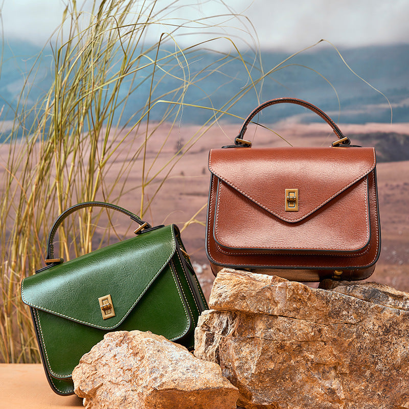 Brown and green leather messenger bags displayed on rocks with desert backdrop